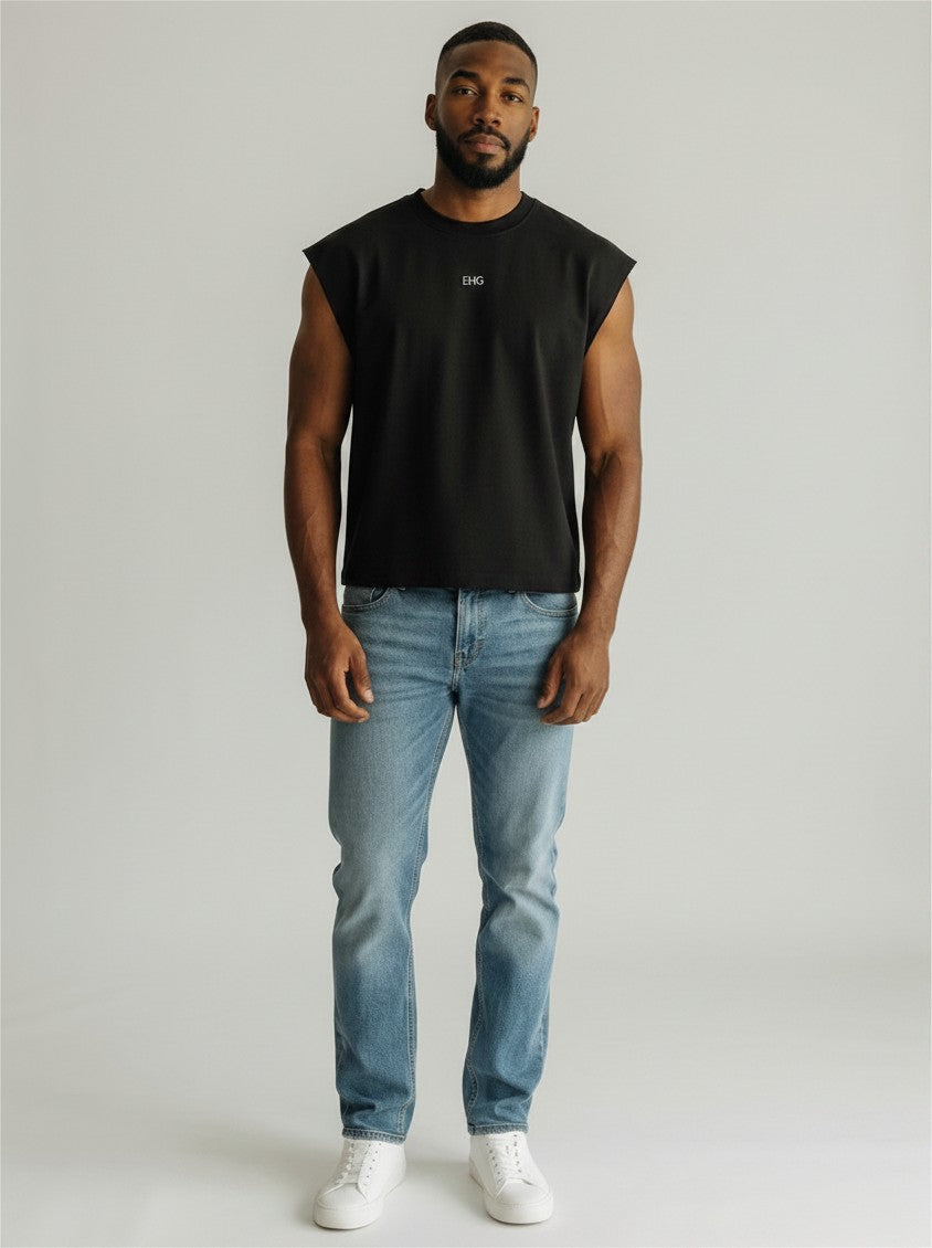 A man wearing an EHG SmartWellness black French terry boxy tank top with a raw hem and blue jeans.