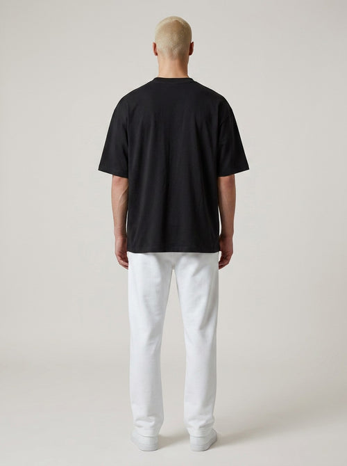 Back view of a man wearing an EHG SmartWellness heavyweight black cotton t-shirt with white trousers.