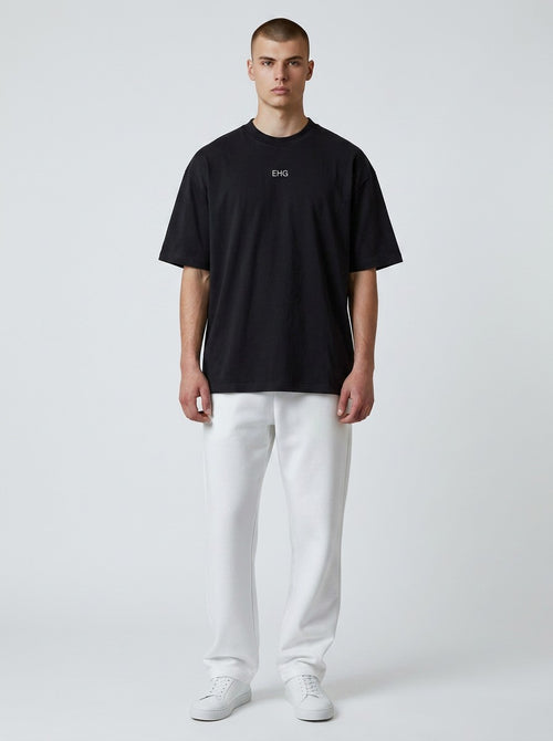 A model wearing an EHG SmartWellness black heavyweight cotton t-shirt with a round neck and white trousers.