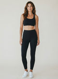 Model wearing EHG SmartWellness black high-waisted shaping ankle leggings and matching sports bra with white sneakers.