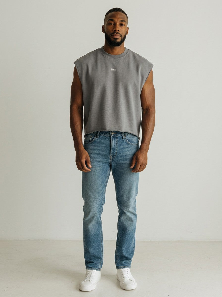 A man wearing an EHG SmartWellness grey French terry boxy tank top with a raw hem, paired with blue jeans and white sneakers.