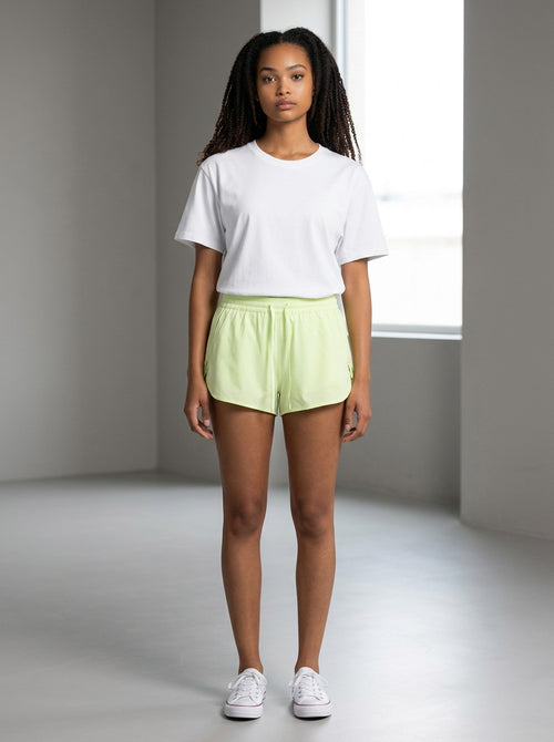 Model wearing EHG SmartWellness lime green Bermuda shorts with a drawstring waist and white t-shirt in a studio.