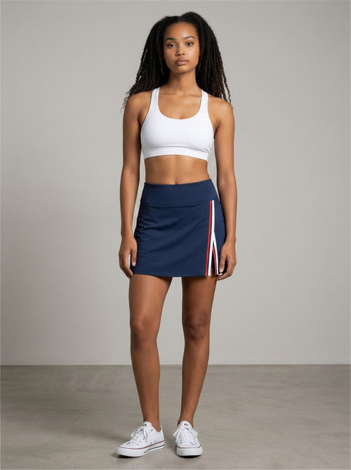 Model wearing EHG SmartWellness navy A-line skirt with contrast side panels and slit, paired with white sports bra.